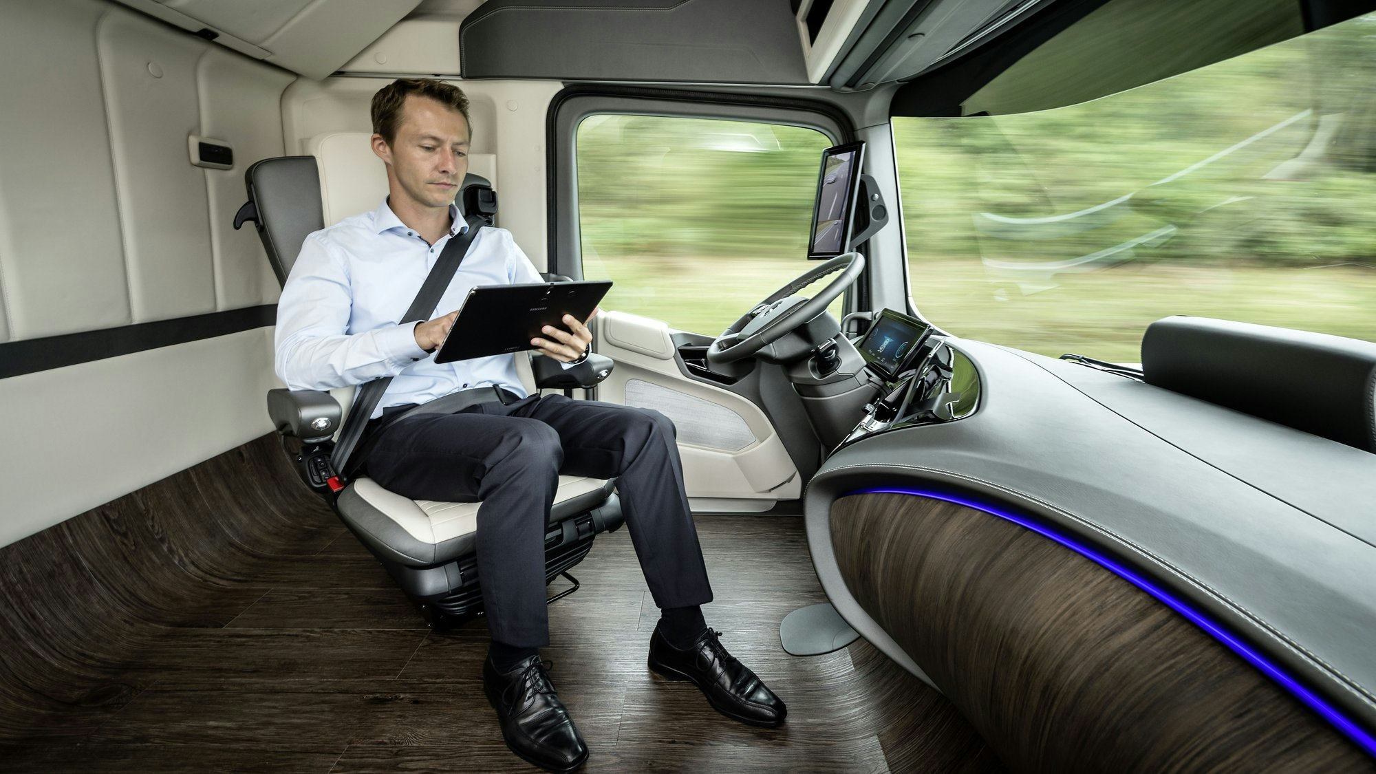 De zelfrijdende Mercedes future truck waarin de chauffeur niet meer zijn handen aan het stuur heeft maar een iPad bediend.