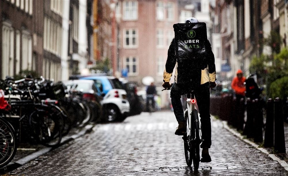 Een fietskoerier van Uber in Amsterdam onderweg met een maaltijd. Volgens Walther Ploos van Amstel wordt het in de hoofdstad, mede door de groei van levensmiddelenbezorging, steeds drukker met busjes van pakketbezorgers. Social delivery op buurtniveau door Buurtmus, ViaTim en Confy moeten de druk doen verminderen.