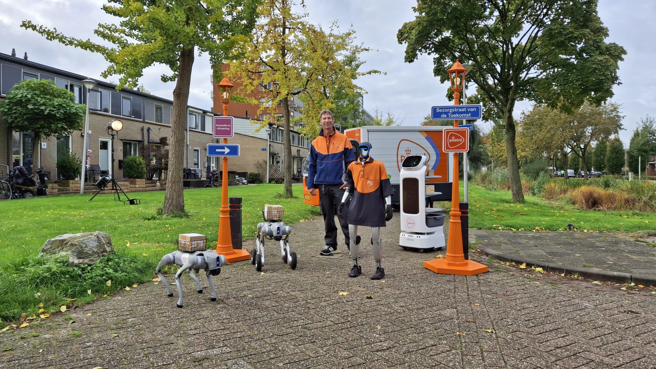 Bezorger Ronald naast twee robothonden, een humanoïde robot en serveerrobot van PostNL. Foto: Logistiek.nl