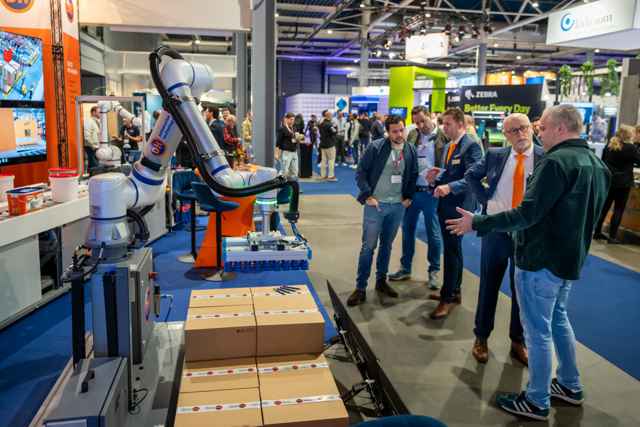 Een cobot van DH Automation Technology palletiseert dozen, terwijl bezoekers de demonstratie volgen.
